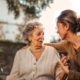 Elderly woman and adult daughter share a joyful, affectionate moment in a sunny garden.