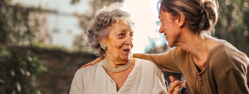 Elderly woman and adult daughter share a joyful, affectionate moment in a sunny garden.