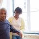 An elderly man receives care from a young woman near a bright window in Portugal.