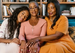 Three beautiful black women sitting together on a couch, smiling indoors.
