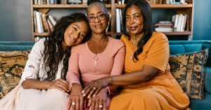 Three beautiful black women sitting together on a couch, smiling indoors.