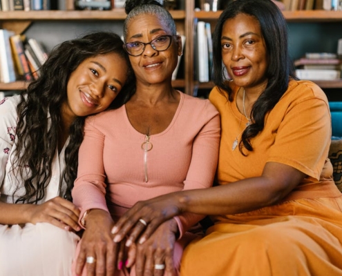 Three beautiful black women sitting together on a couch, smiling indoors.