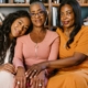 Three beautiful black women sitting together on a couch, smiling indoors.
